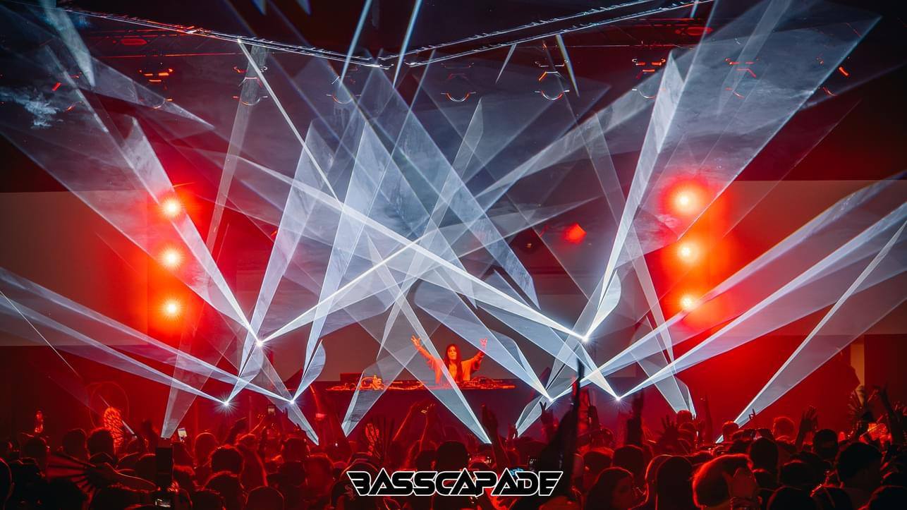 White laser beams crossing a red-lit stage above the DJ
