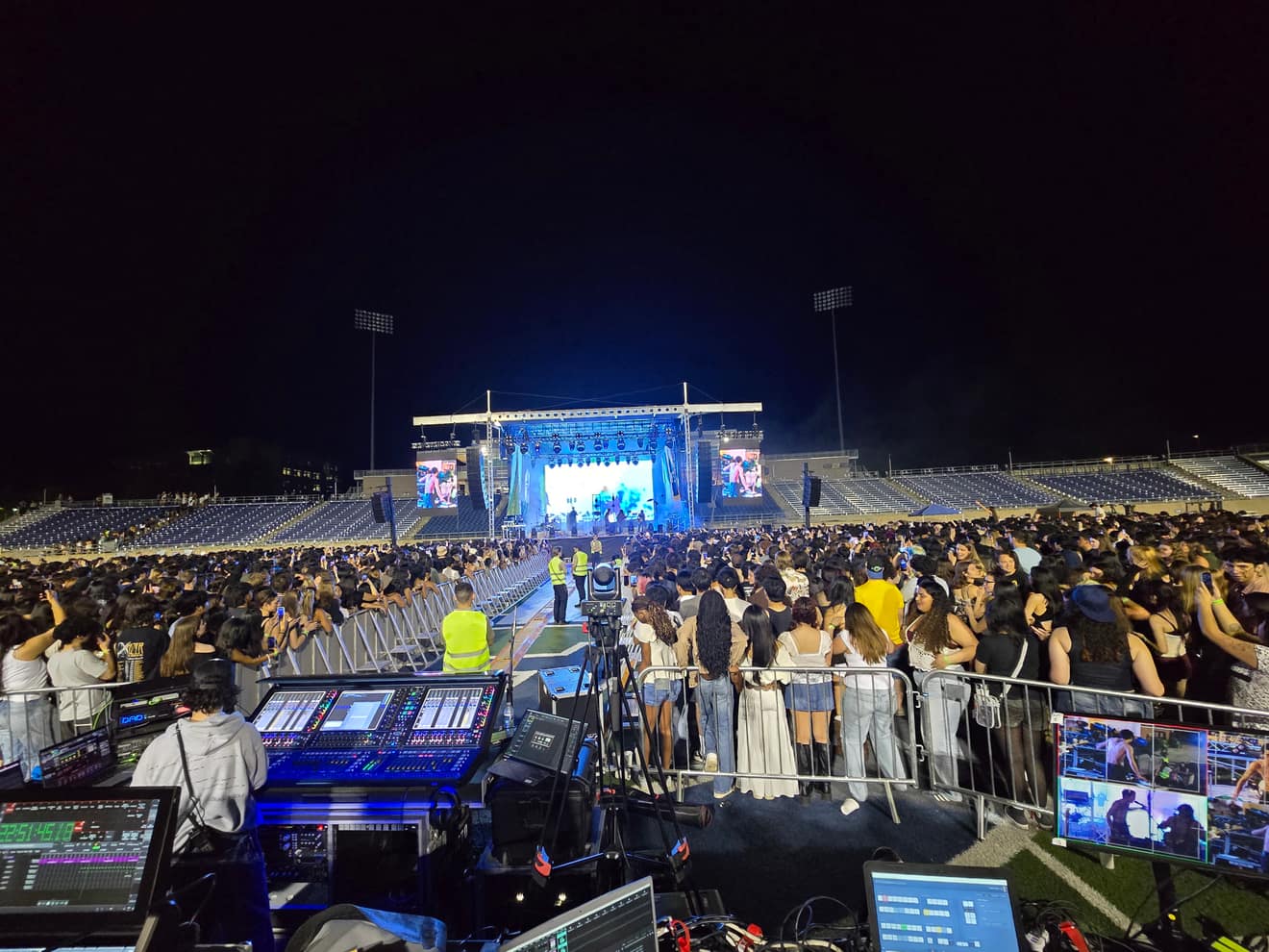 Front of house at a stadium show: audio desk, camera monitors carrying the live iMag feeds