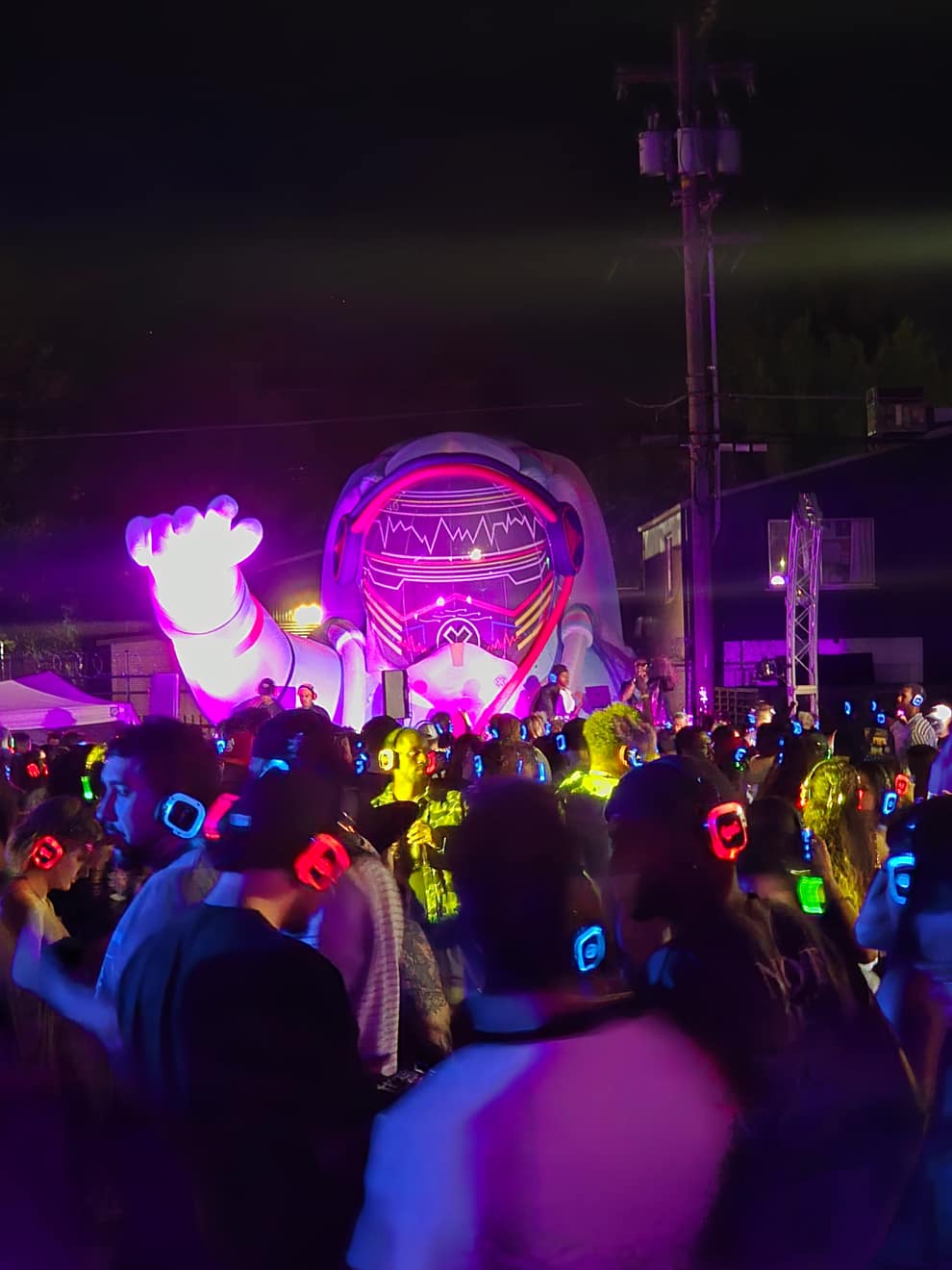 The astronaut inflatable up close over a dense crowd in LED headphones