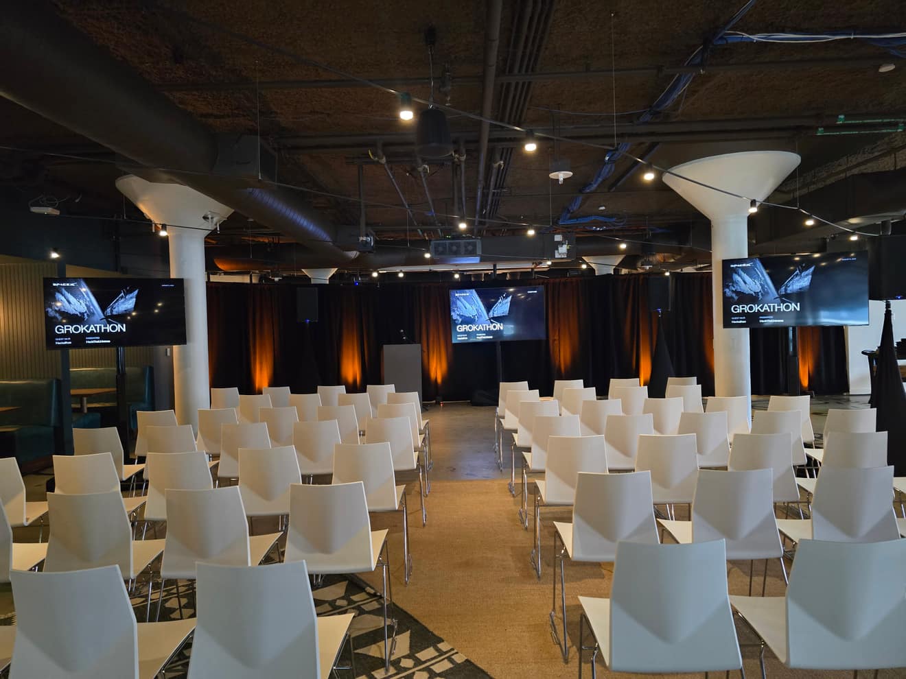 Session room set for a corporate hackathon: three screens, uplit drape, rows of seating
