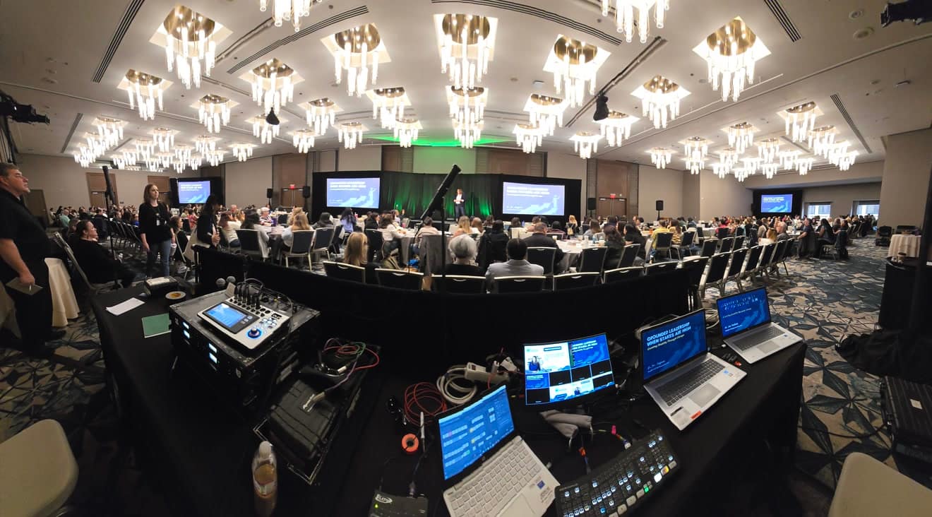 Ballroom general session under chandeliers, three screens on stage