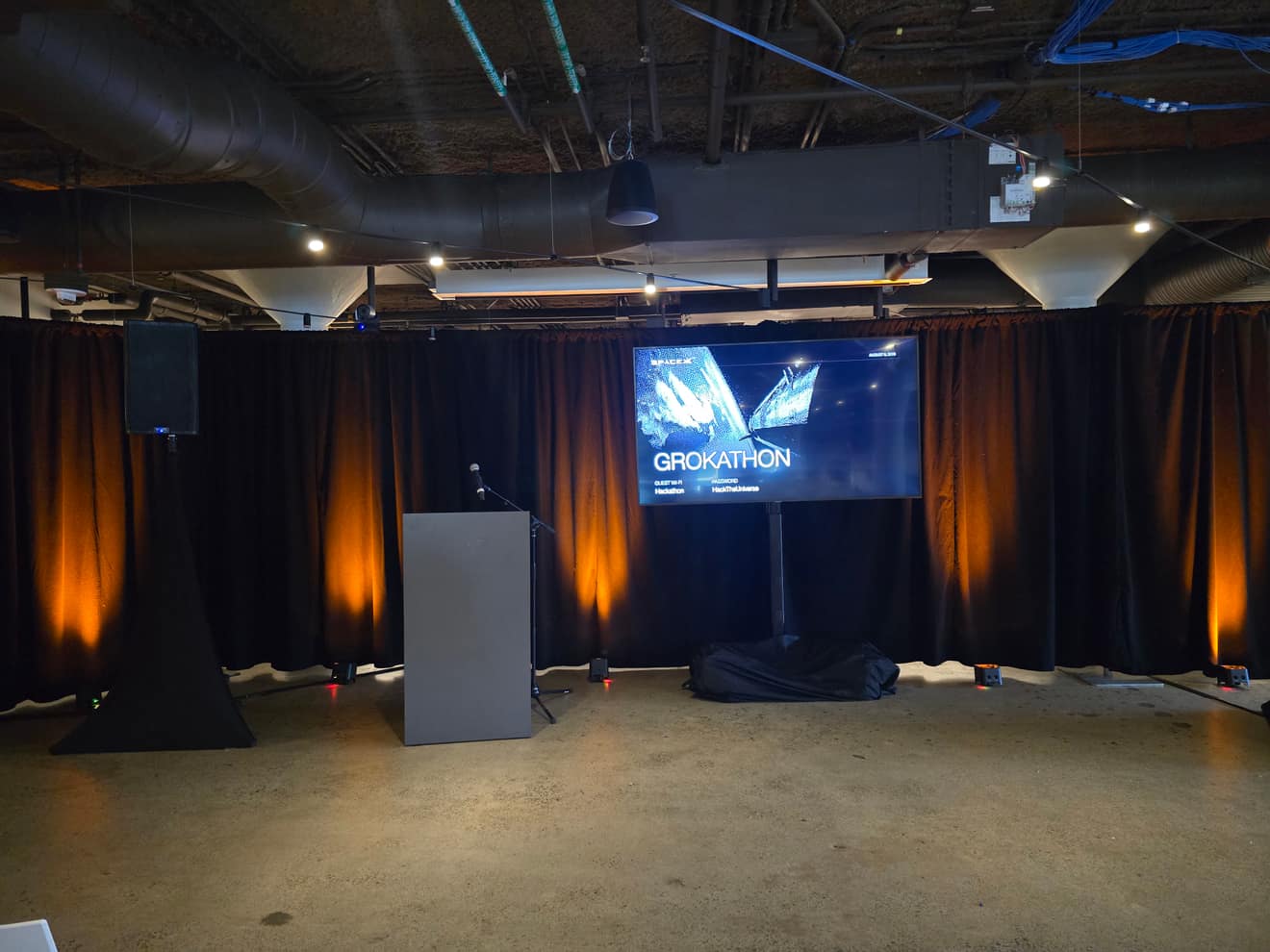 Main stage and screen at the SpaceX hackathon, orange uplight on drape